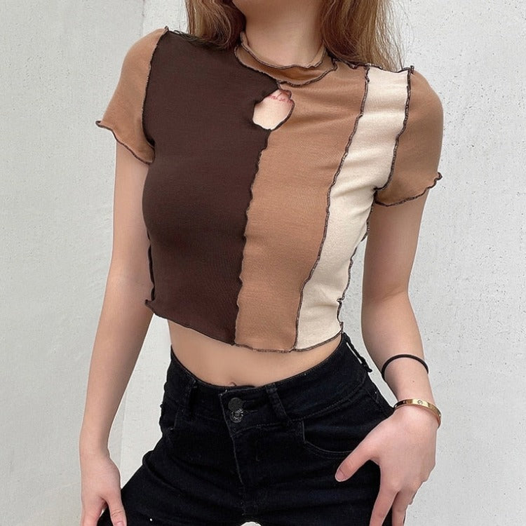 Brown Tan Cream Crop Top – Retro Y2K Aesthetic Top. A woman wearing a short-sleeve knit crop top with vertical color-block panels in dark brown, tan, and cream, featuring a ruffled edge and a small chest cutout. She is also wearing black jeans against a light gray wall.