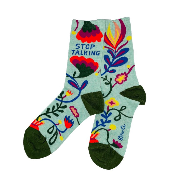 Stop Talking Socks – Mint Green Floral Y2K Crew Socks. A pair of light mint green crew socks with a colorful folk-art floral pattern and dark green heels, toes, and soles. One sock features the text 'STOP TALKING' in blue