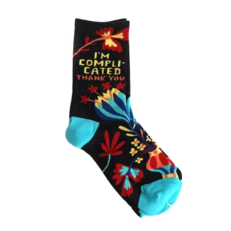 I’m Complicated Socks – Colorful Floral Y2K Crew Socks.  black crew socks with a colorful floral pattern and the text 'I'M COMPLICATED THANK YOU' in yellow and red, featuring bright turquoise blue heels and toes.