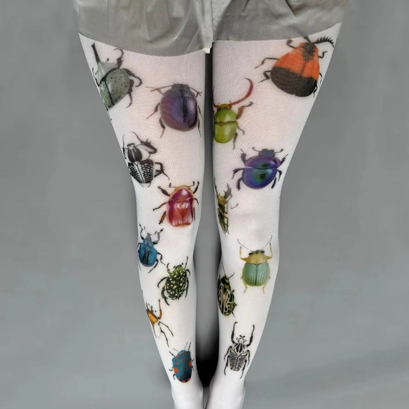 Insect Print Tights - Quirky Aesthetic Tights. White tights with a colorful printed pattern of various beetles and bugs, shown on a model's legs against a plain gray background.
