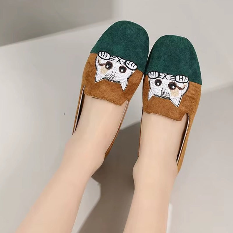 Cute Cat Loafers – Brown Suede Aesthetic Shoes. A pair of women's flat shoes being worn, featuring a dark green suede upper, a brown suede lower section, and a white embroidered cat face motif on the toe area.