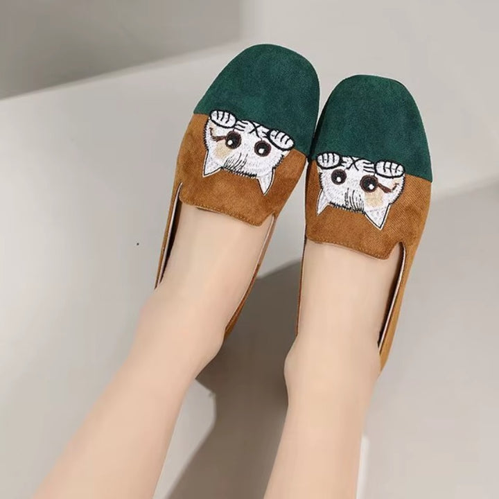 Cute Cat Loafers – Brown Suede Aesthetic Shoes. A pair of women's flat shoes being worn, featuring a dark green suede upper, a brown suede lower section, and a white embroidered cat face motif on the toe area.