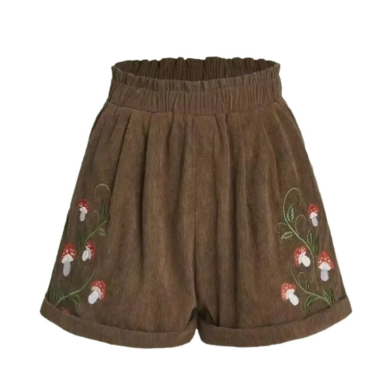 Cottagecore Mushroom Shorts – Cottagecore Aesthetic Clothing. Brown corduroy shorts with an elastic waistband and embroidered red-and-white mushrooms with green stems on both sides.