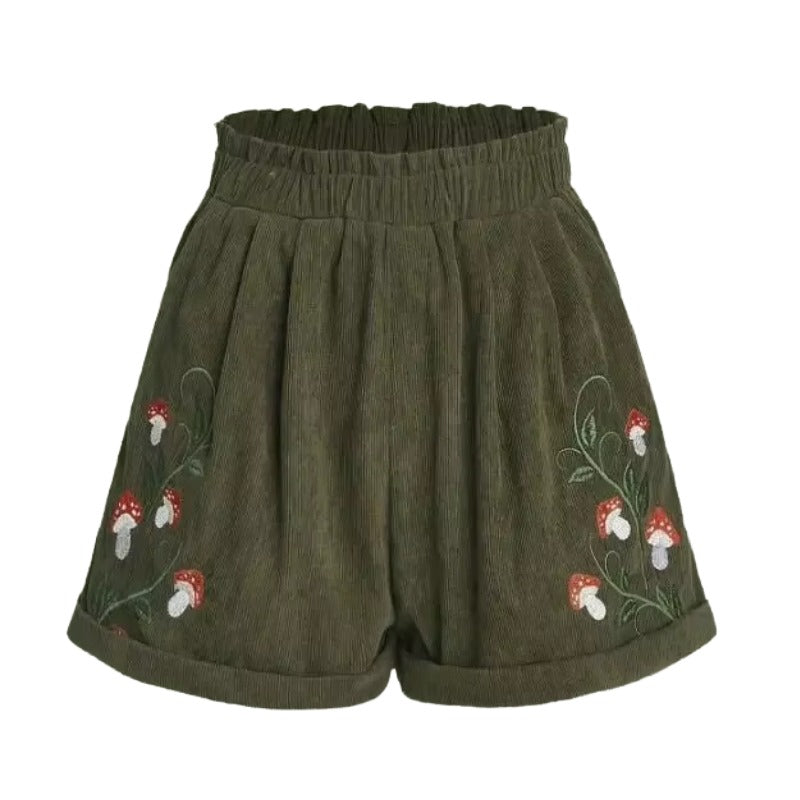 Cottagecore Mushroom Shorts – Cottagecore Aesthetic Clothing. Olive green corduroy shorts with an elastic waistband and embroidered red and white mushrooms with green stems on both sides, shown against a plain white background.